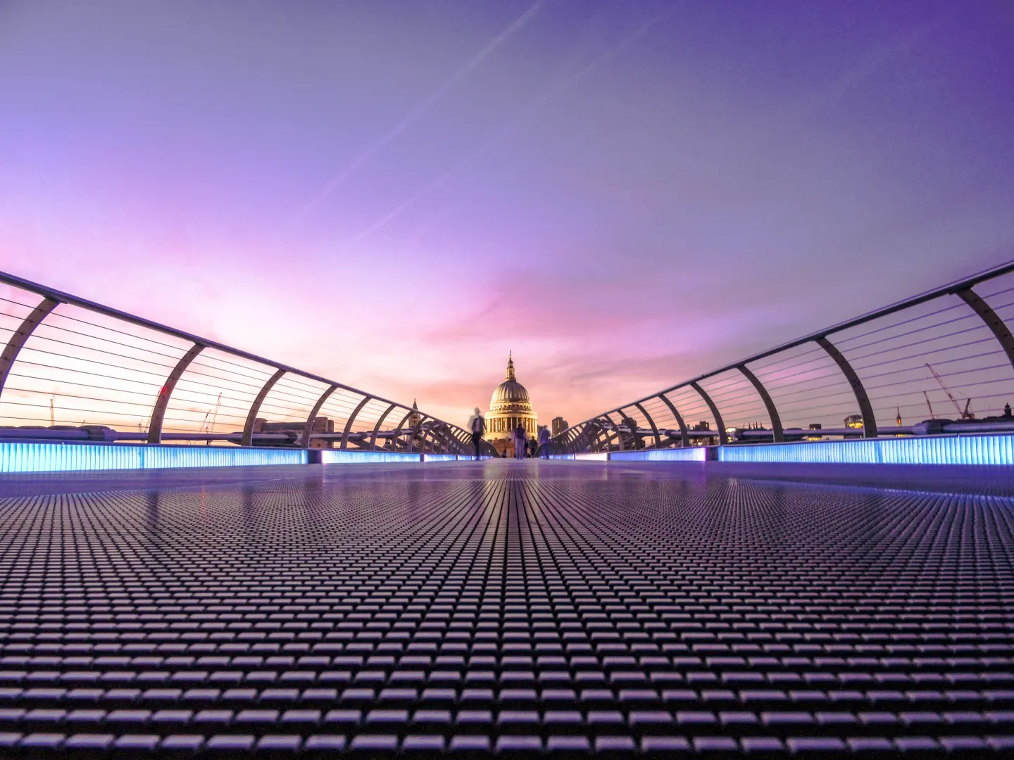 A walk across Millennium Bridge towards St Paul's Cathedral, with blue-lit railings and a pink evening sky